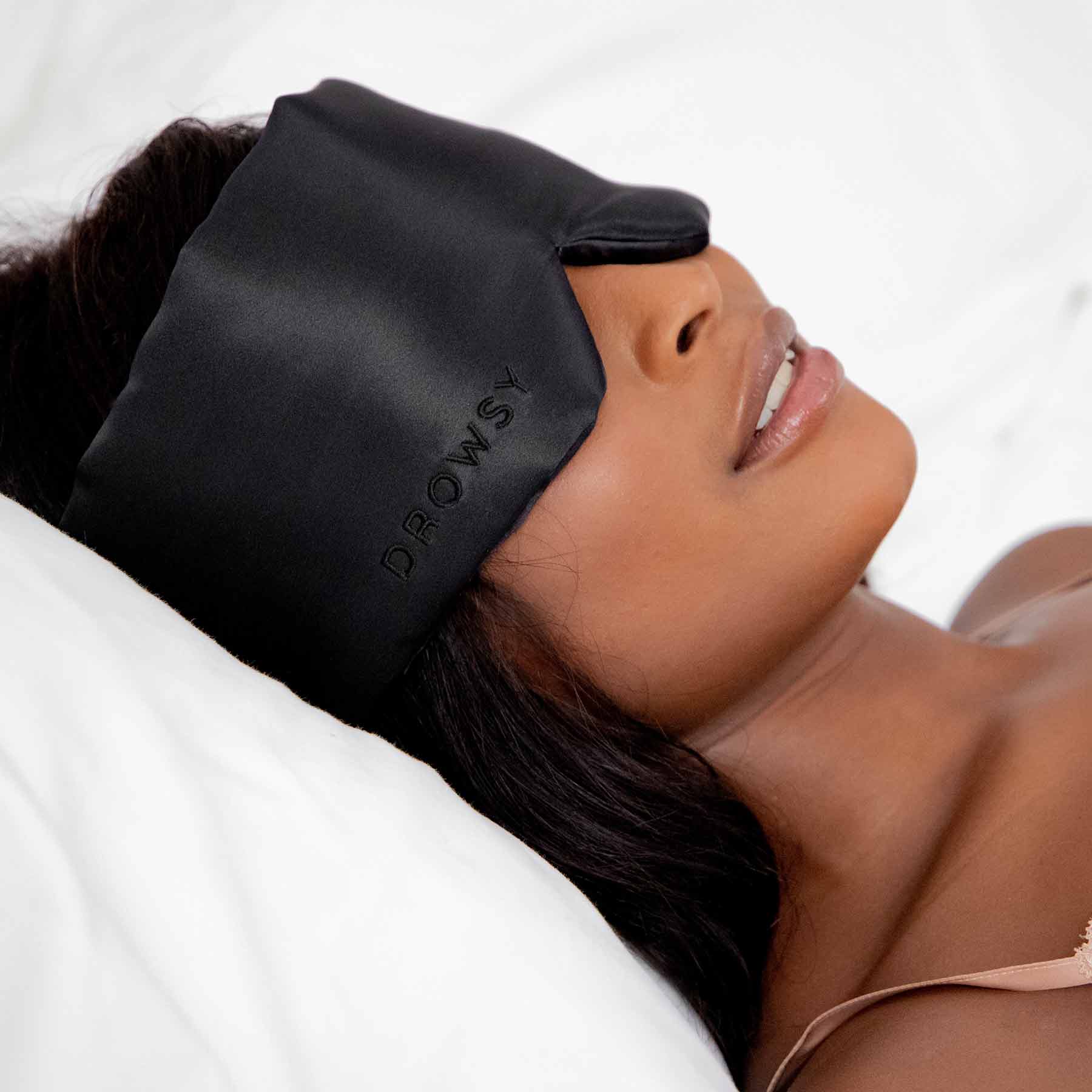 Person wearing a black sleep mask with 'Drowsy' branding on a white background