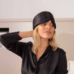 Woman wearing a black satin sleep mask indoors.