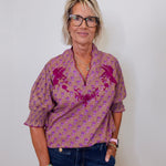 Woman wearing a patterned shirt and jeans against a plain background