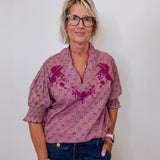 Woman wearing a patterned shirt and jeans against a plain background