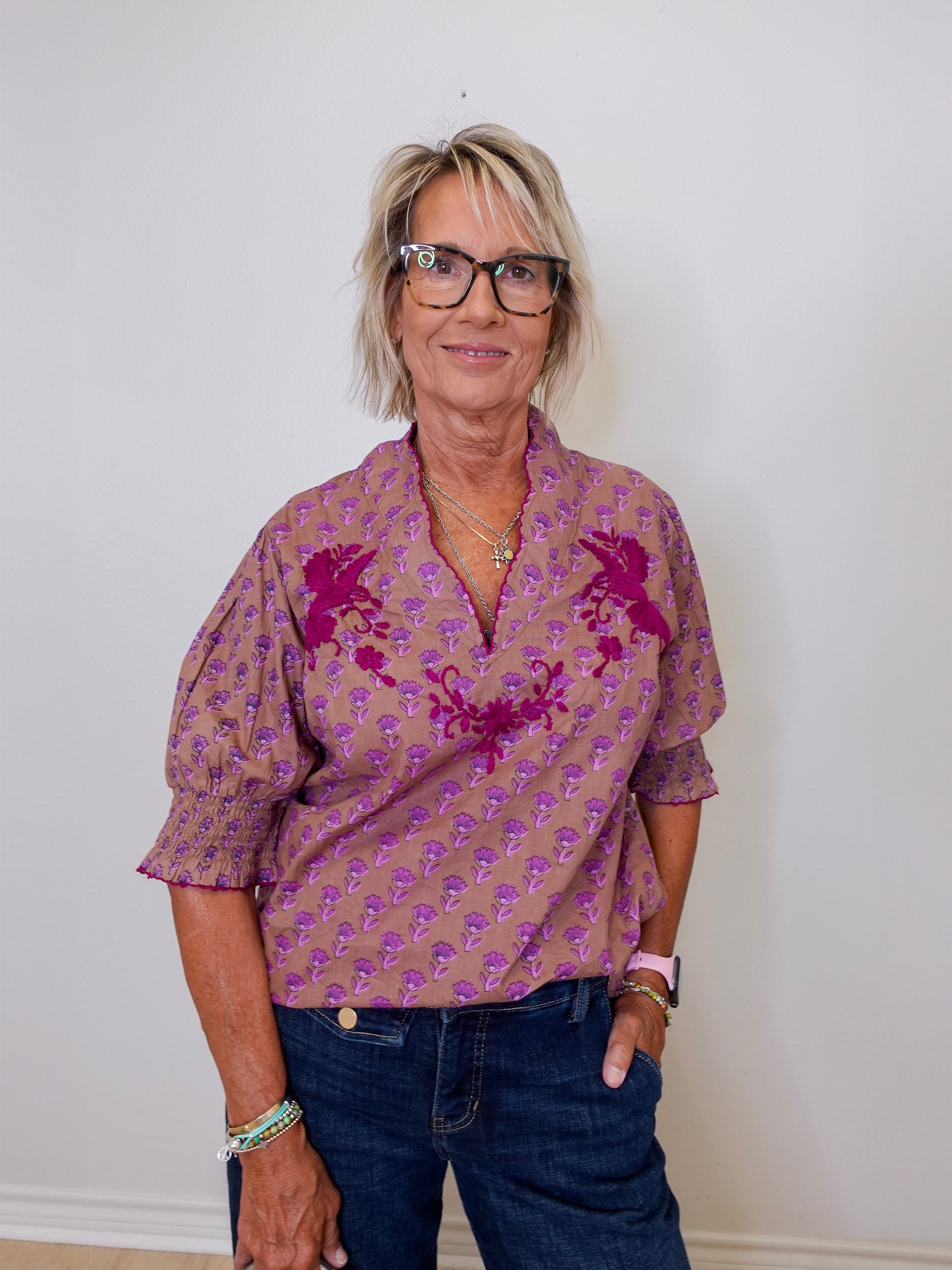 Woman wearing a patterned shirt and jeans against a plain background