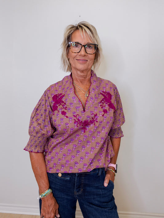 Woman wearing a patterned shirt and jeans against a plain background