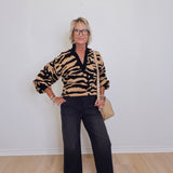 Person wearing a tiger-striped sweater and black pants against a white wall.