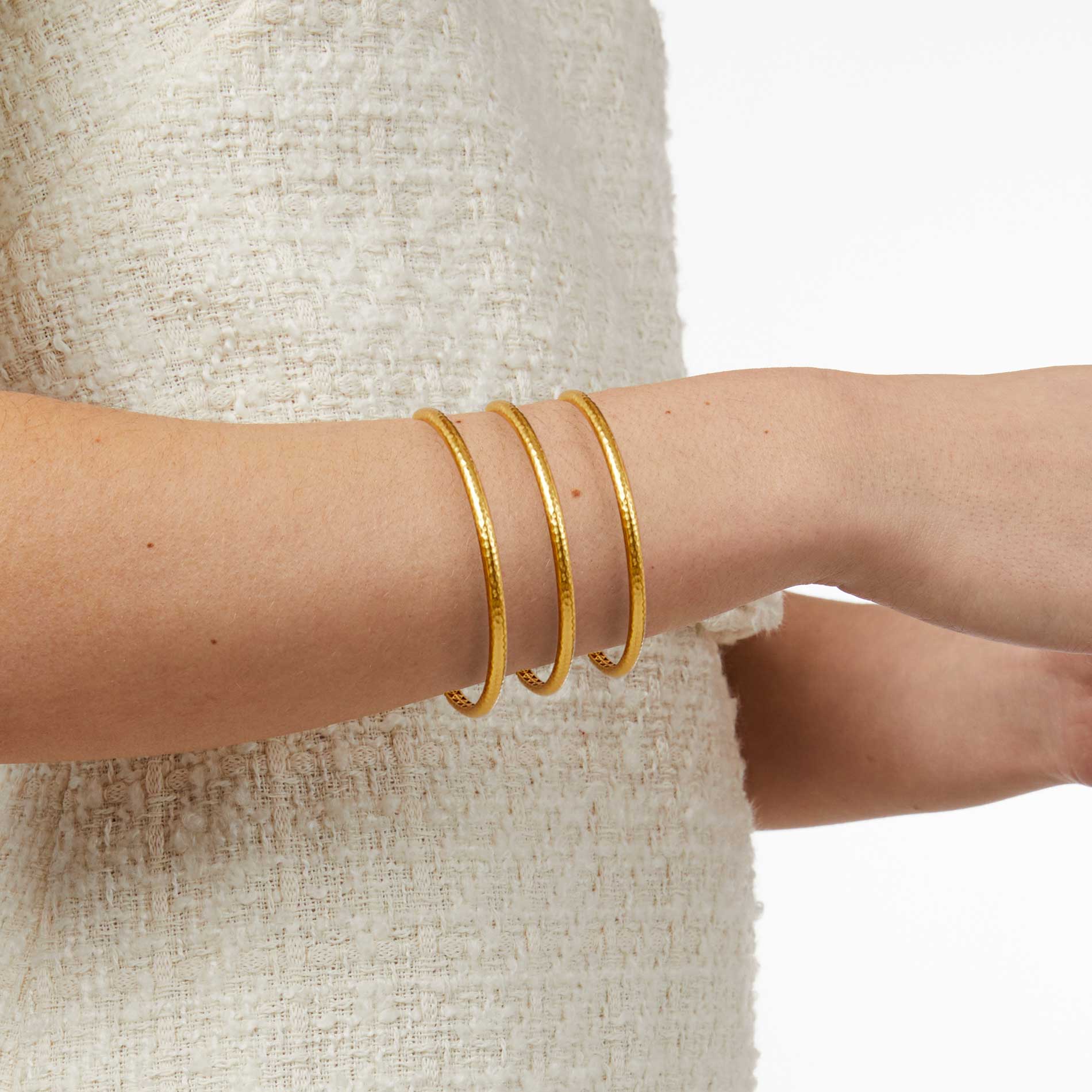 Gold bangles on a person's wrist with a neutral background