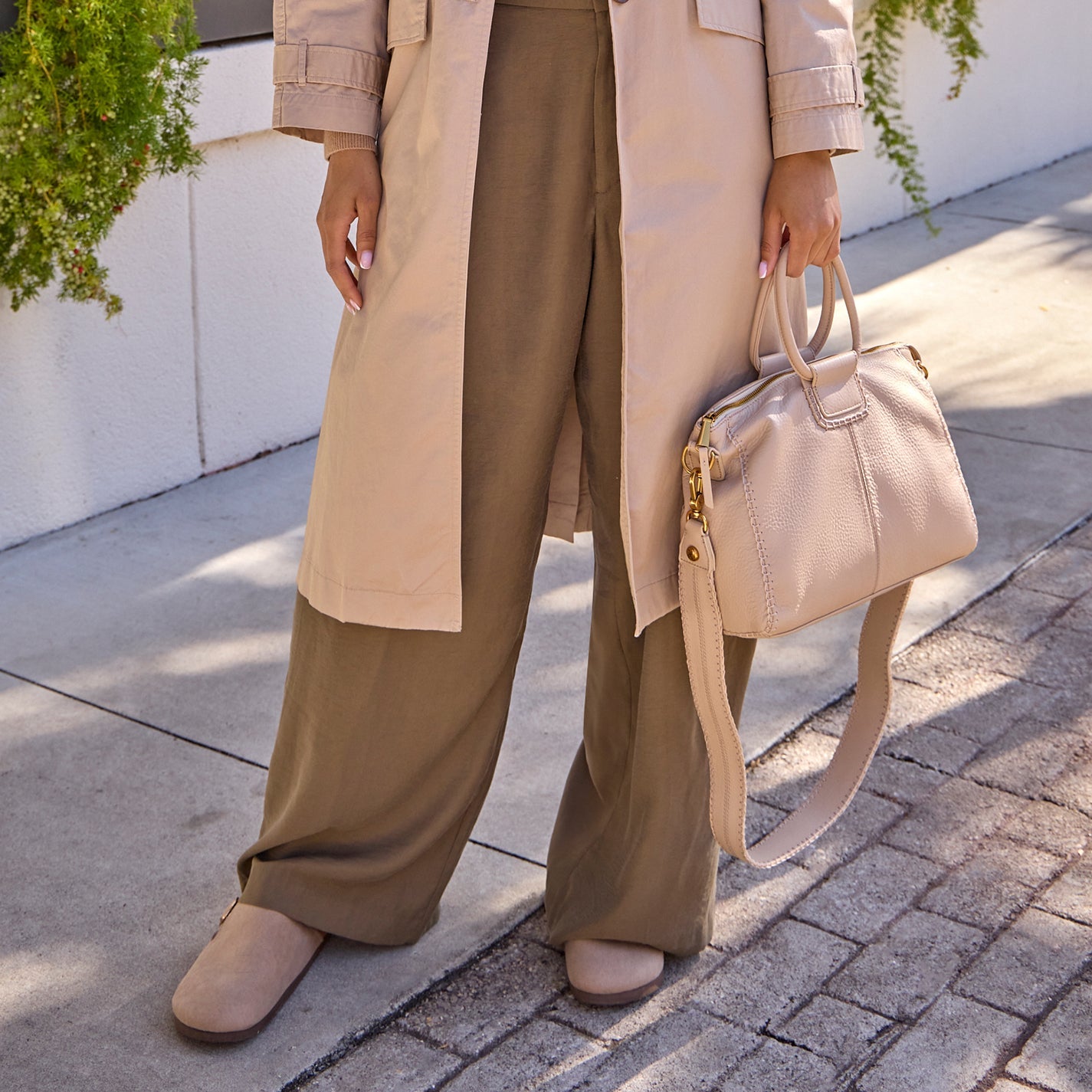 Person wearing a beige trench coat and holding a matching handbag on a sidewalk.
