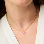 Gold necklace with a pink heart pendant worn by a person
