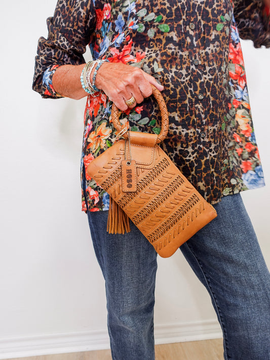 Person holding a brown woven handbag with a patterned top and jeans.