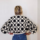 Person wearing a black and white checkered jacket with balloon sleeves against a plain background