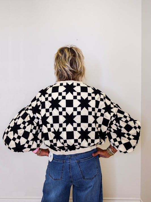 Person wearing a black and white checkered jacket with balloon sleeves against a plain background