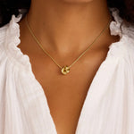Gold necklace with a pendant worn by a person in a white blouse