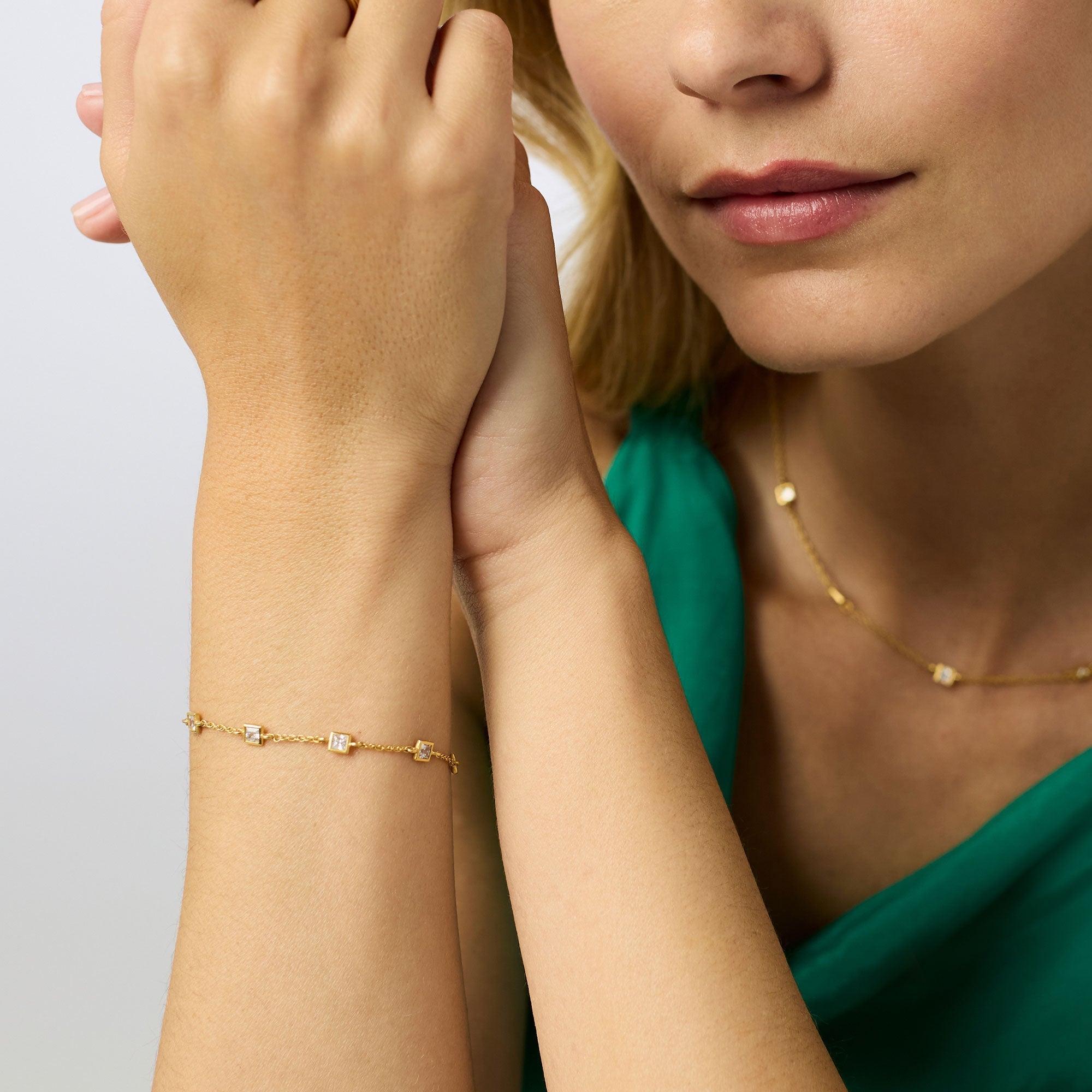 Woman wearing a gold bracelet and necklace on a neutral background
