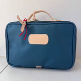 Blue toiletry bag with beige handle and patch on a white background