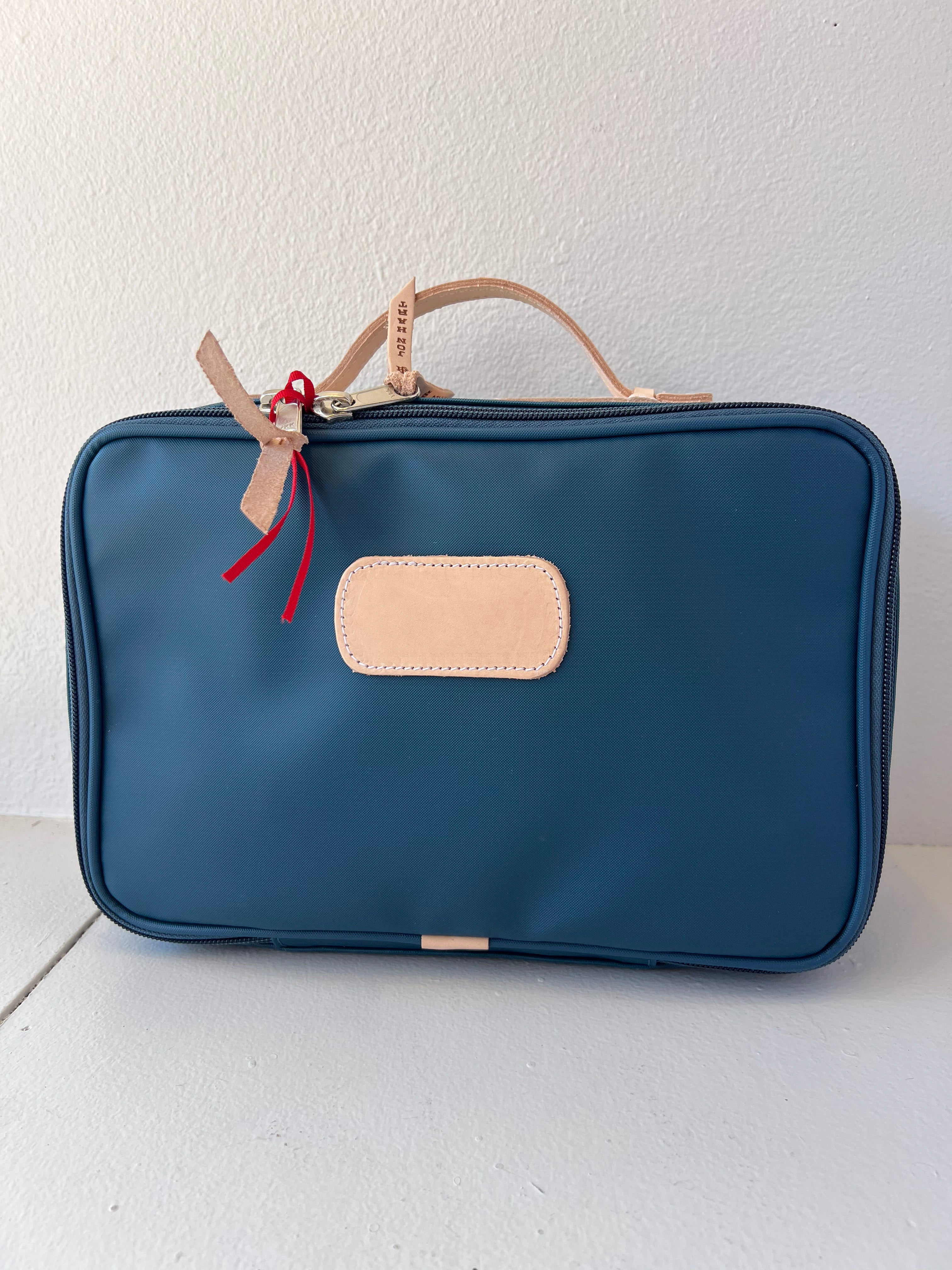 Blue toiletry bag with beige handle and patch on a white background