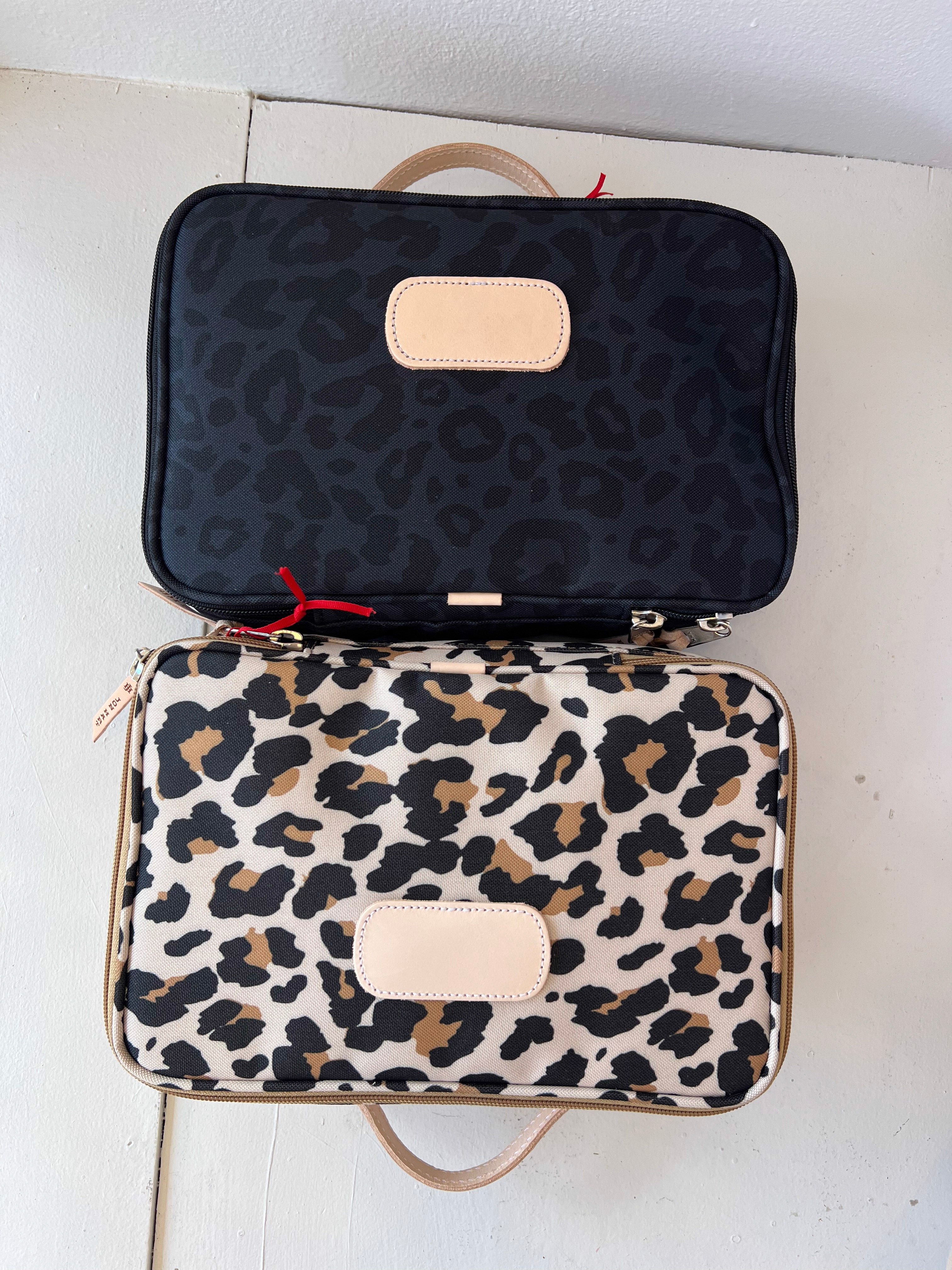 Two patterned bags, one black with leopard print and the other white with brown leopard print, on a light background.