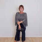 Woman wearing a gray sweater and black pants against a white wall.