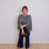 Woman wearing a gray sweater and black pants against a white wall.