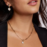 Close-up of a person wearing a gold chain necklace with a heart pendant.