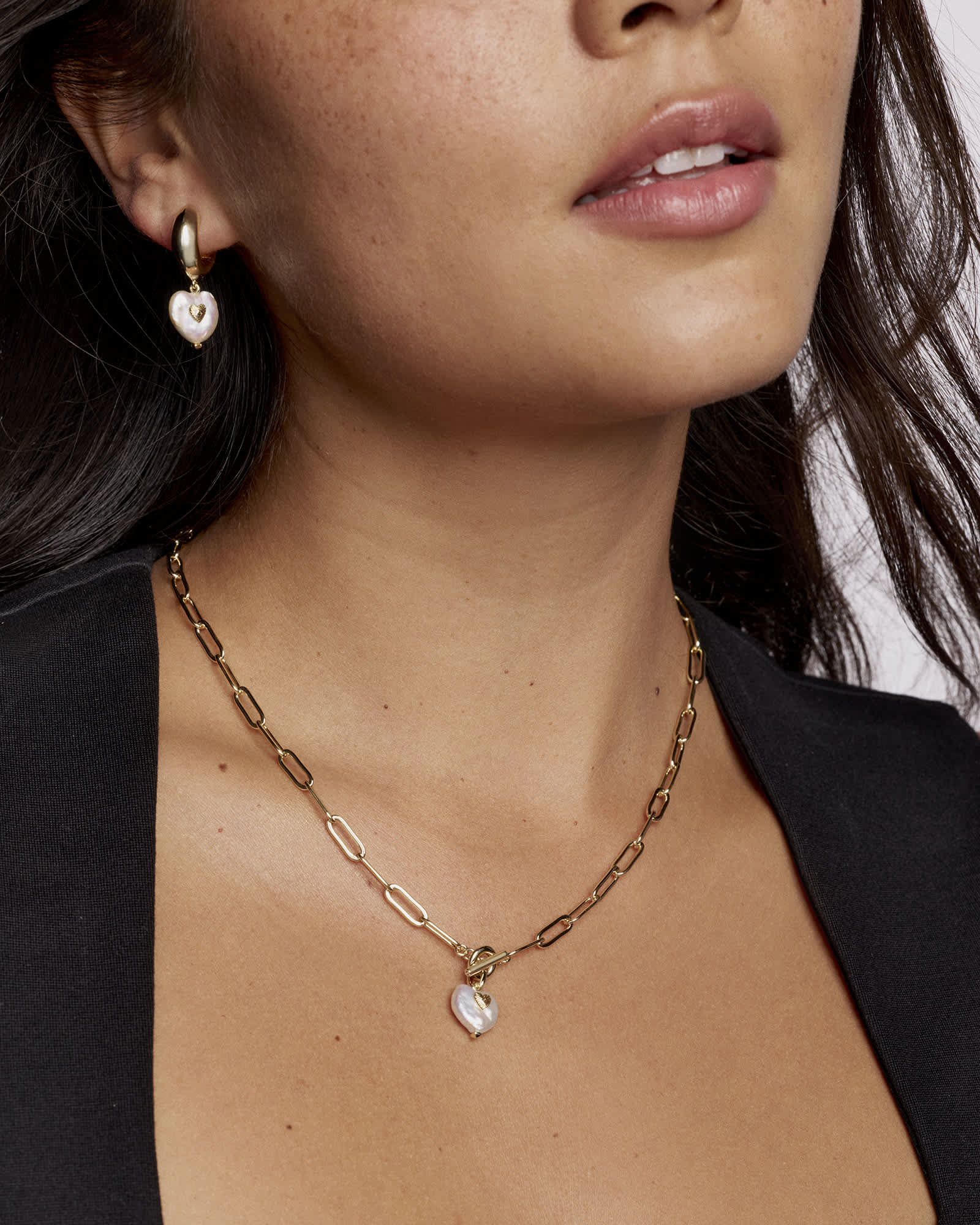 Close-up of a person wearing a gold chain necklace with a heart pendant.