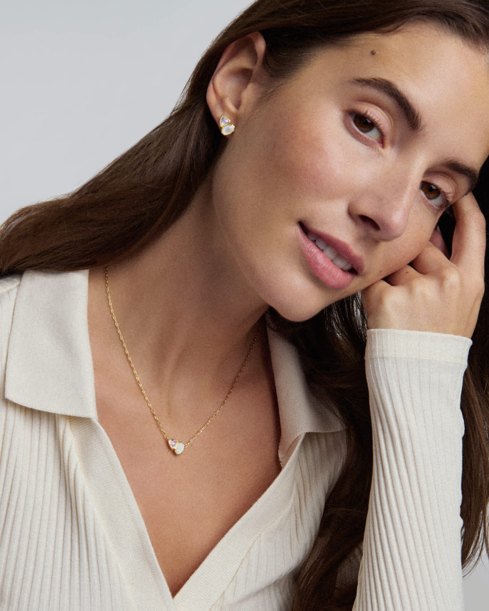 Woman wearing a gold necklace and earrings against a neutral background