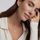 Woman wearing a gold necklace and earrings against a neutral background