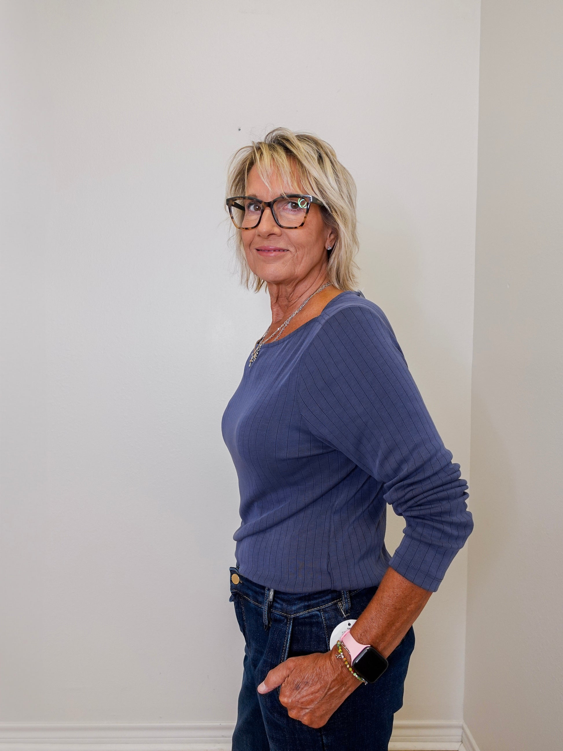 Woman wearing a blue sweater and glasses against a white wall