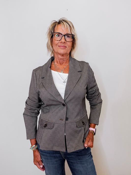 Woman wearing a camel blazer over a white shirt with a plain background