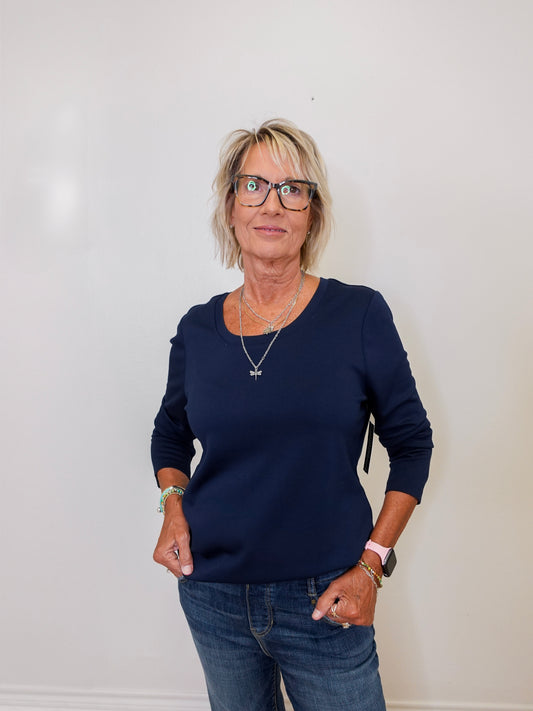 Woman wearing a navy top and jeans against a white background