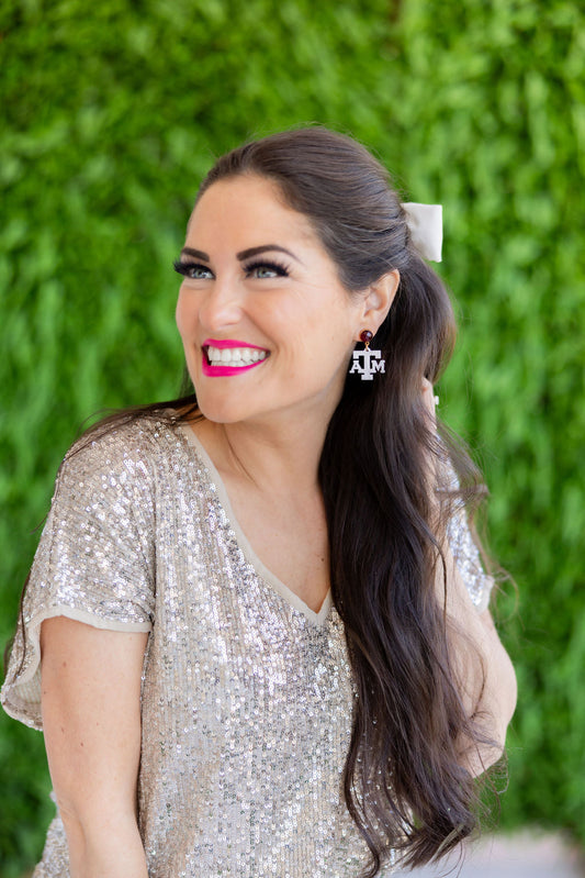 Woman with long dark hair wearing a sequin top in front of a green hedge