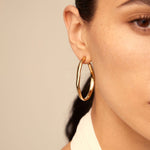 Close-up of a person wearing gold hoop earrings with a neutral background