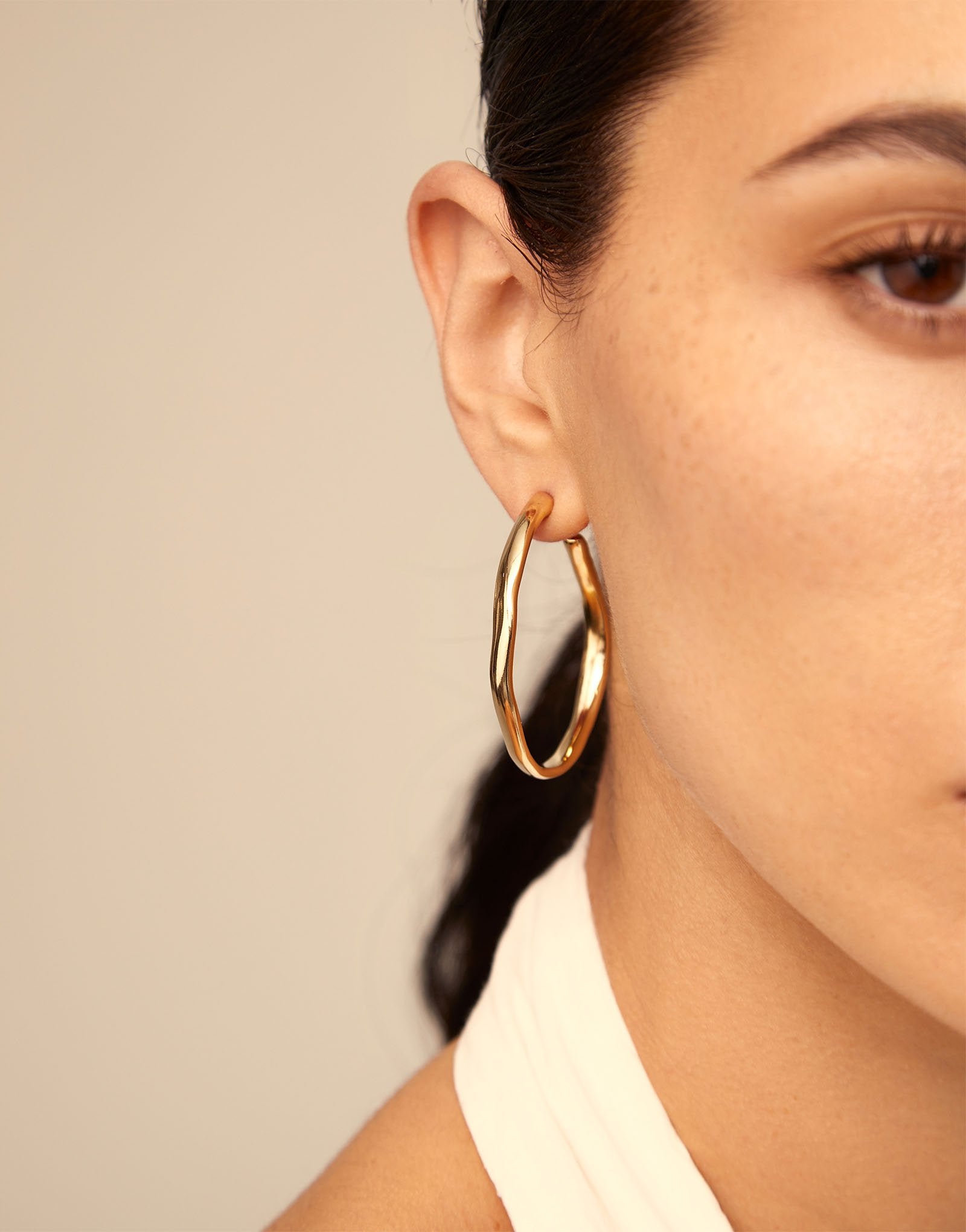 Close-up of a person wearing gold hoop earrings with a neutral background