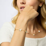 Close-up of a woman's hand wearing a gold bracelet with heart charms, against a neutral background.