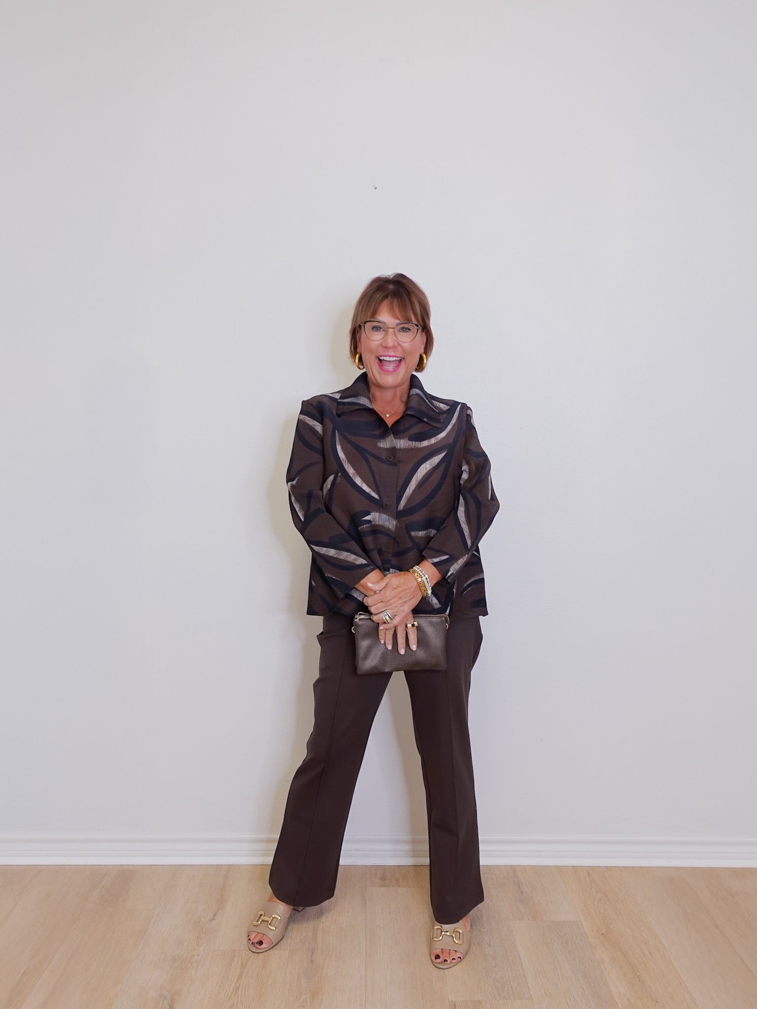 Woman wearing a patterned jacket and dark pants against a white wall.