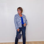 Woman standing against a white wall wearing a blue plaid jacket, blue shirt, and jeans.
