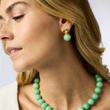 Woman wearing a green beaded necklace and earrings against a white background