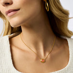 Close-up of a woman wearing a gold necklace with a pink pendant on a neutral background