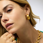 Close-up of a woman wearing gold hoop earrings and a gold necklace with a white background