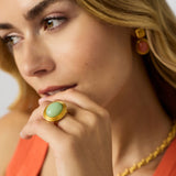 Close-up of a woman wearing a gold ring with a green gemstone and matching earrings.