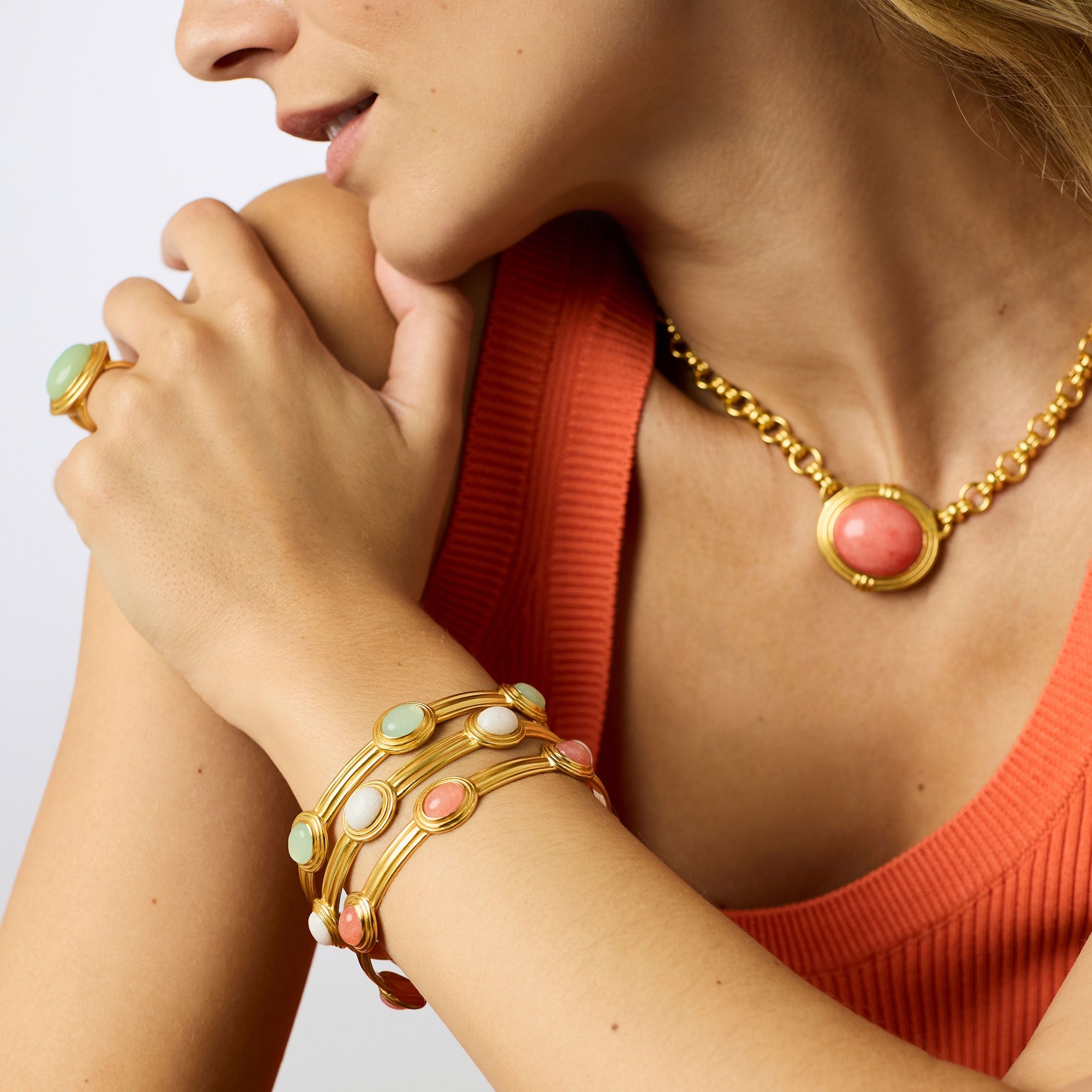 Woman wearing gold jewelry with pink stones on a plain background