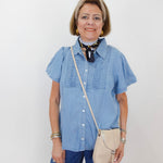 Woman wearing a blue shirt and jeans with a beige crossbody bag against a white background
