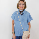 Woman wearing a blue shirt and jeans with a beige crossbody bag against a white background