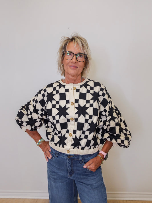Person wearing a black and white patterned cardigan with blue jeans against a plain background