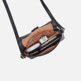 Black handbag with a shoulder strap, open to reveal cosmetic items on a light gray background