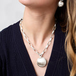 Silver chain necklace with a pendant worn by a person against a neutral background
