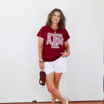 Woman wearing a red t-shirt with a logo and white shorts, standing against a white wall.
