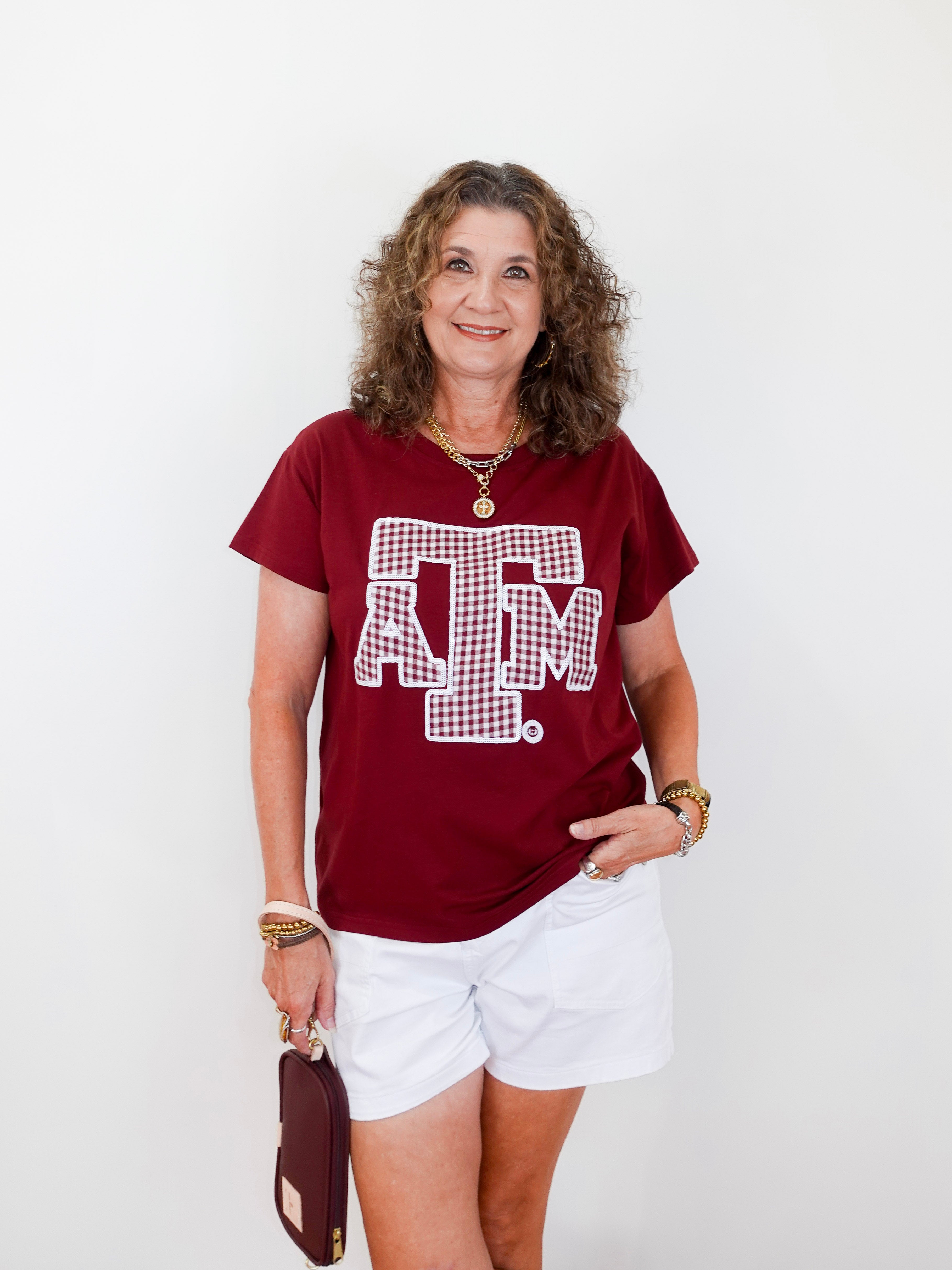 Woman wearing a red t-shirt with a logo and white shorts, holding a brown bag on a white background
