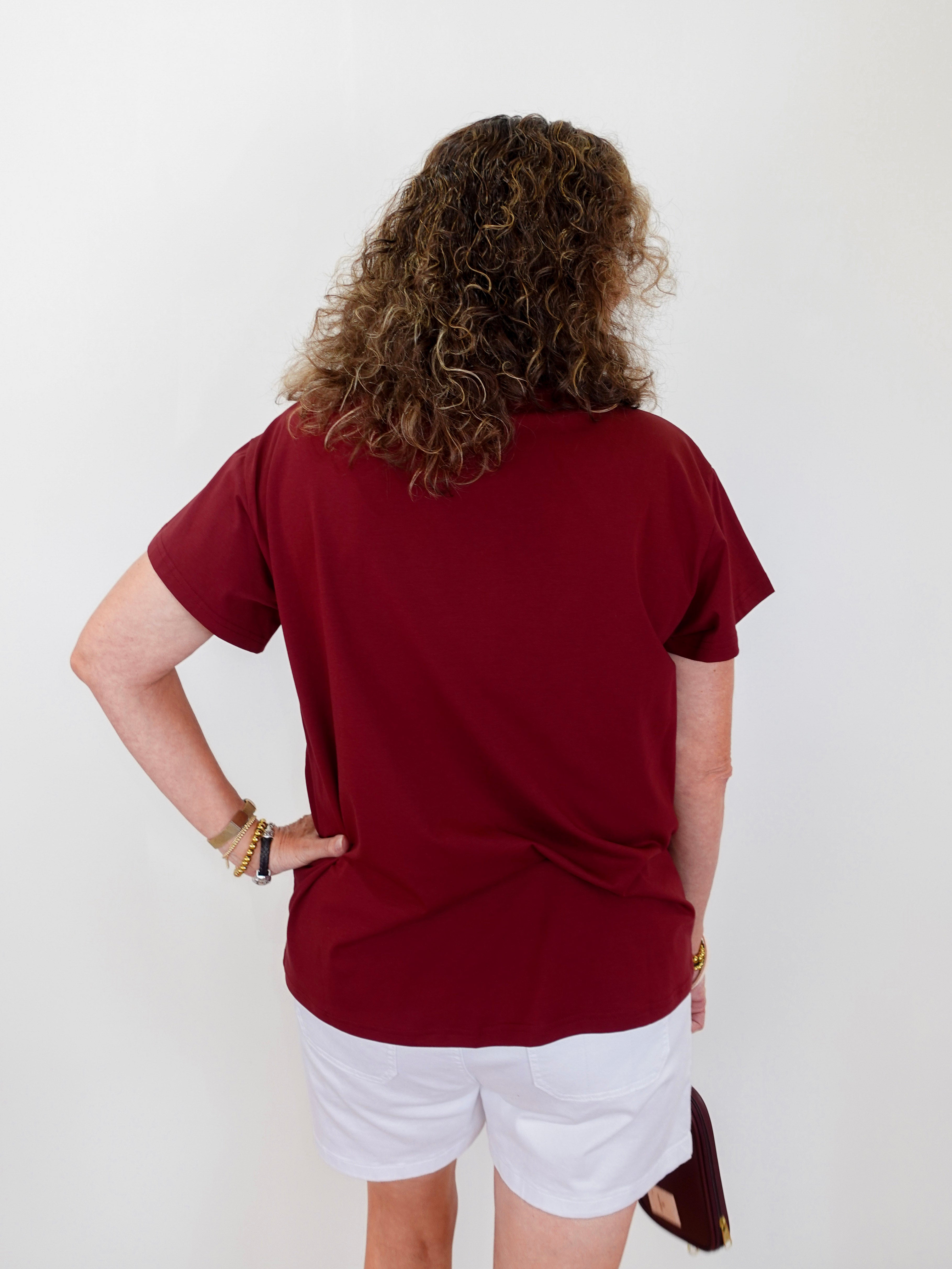 Person wearing a red shirt and white shorts against a plain background