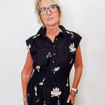 Woman wearing a black dress with white floral patterns against a plain background