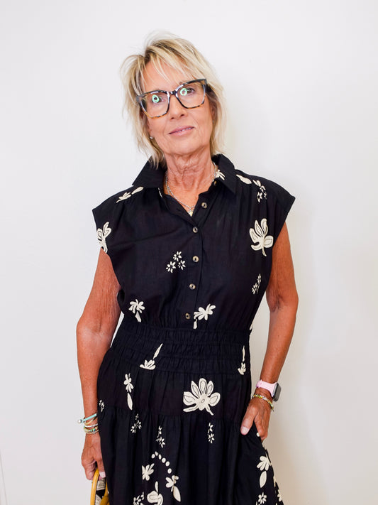 Woman wearing a black dress with white floral patterns against a plain background