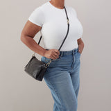 Person wearing a white t-shirt and blue jeans holding a black handbag against a plain background