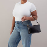 Person wearing a white t-shirt and blue jeans holding a black handbag against a plain background